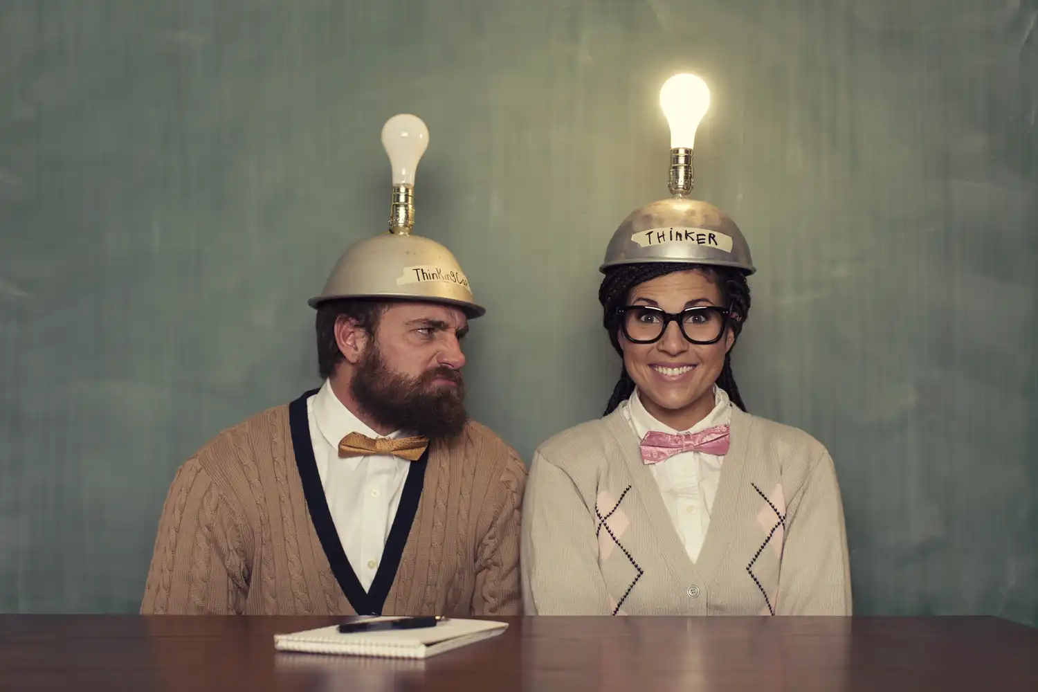 Two people sitting with metal bowls on their heads with lightbulbs on top and the word thinker written across the top.